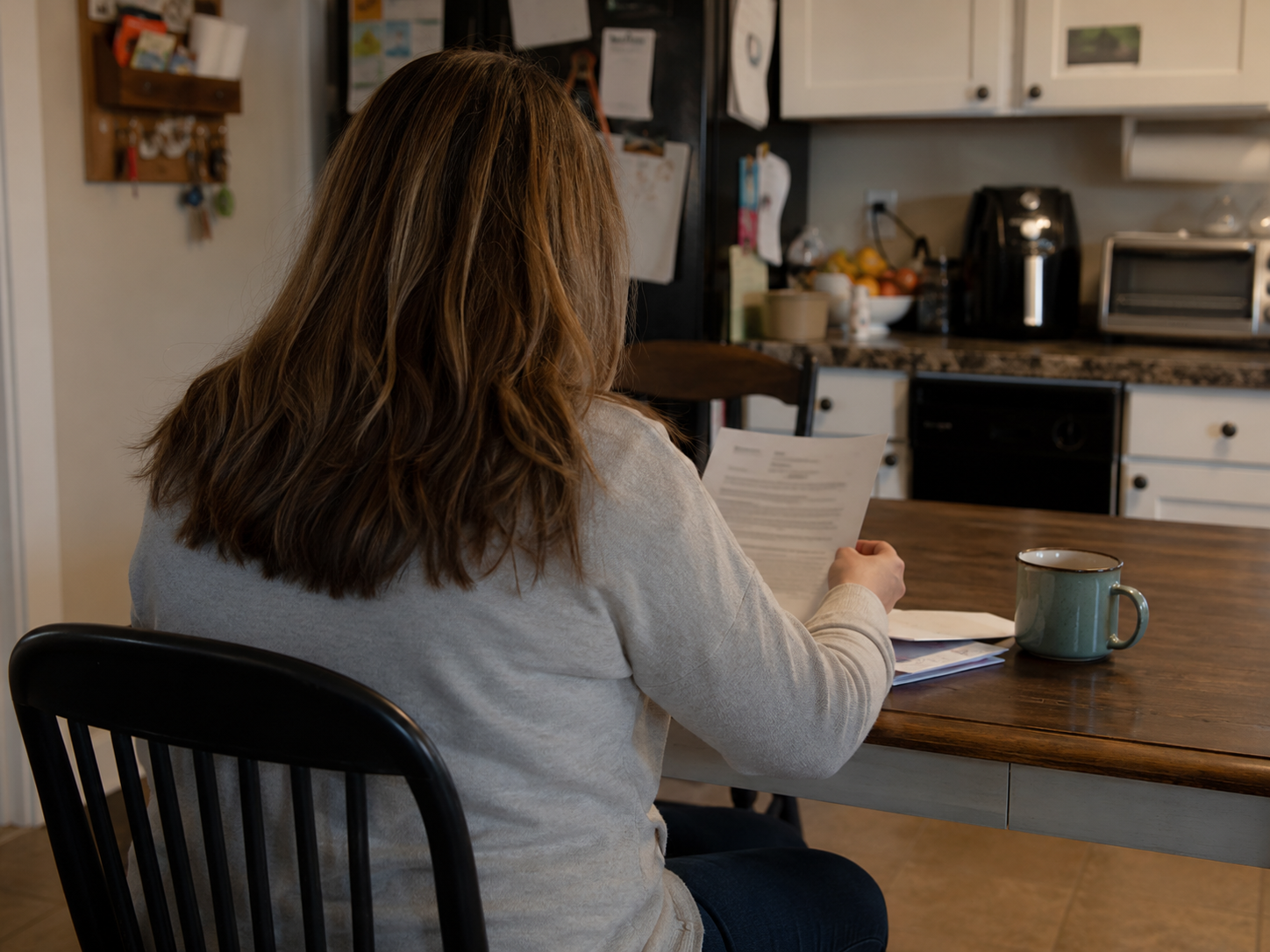 A military spouse seated at a kitchen table reading a document, viewed from behind.